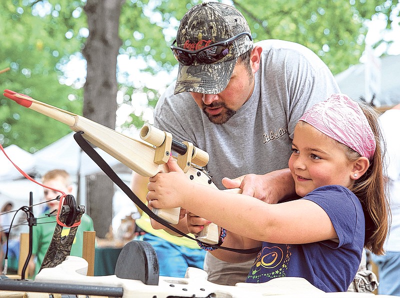 Jody Jones helps his daughter Kalle, 6, shoot a rubber band gun at the Fun Guns booth at the Strawberry Festival in Dayton, Tenn. The booth allowed customers to try out a variety of rubber band guns before making a purchase.