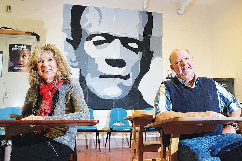 Olga de Klein and Bill Weaver sit in a classroom wall in the Juvenile Detention Center at Hamilton County Juvenile Court in front of a mura painted by juvenile detainees.