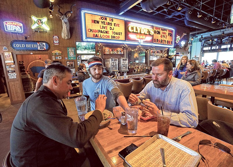 Chris "C-Moore" Glascock refills water as Manuel Abello, left, and Scott Williams eat lunch at Clydes on Main.