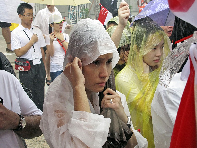 
              Standing in a downpour, Singaporeans wait for the carriage carrying the coffin of Lee Kuan Yew to pass during the funeral procession, Sunday, March 29, 2015, at City Hall in Singapore. Tens of thousands of Singaporeans undeterred by heavy rains lined a 15 kilometer (9 mile) route through the Southeast Asian city-state to witness an elaborate funeral procession Sunday for longtime leader Lee Kuan Yew, who died Monday at 91. (AP Photo/Jeanette Tan)
            