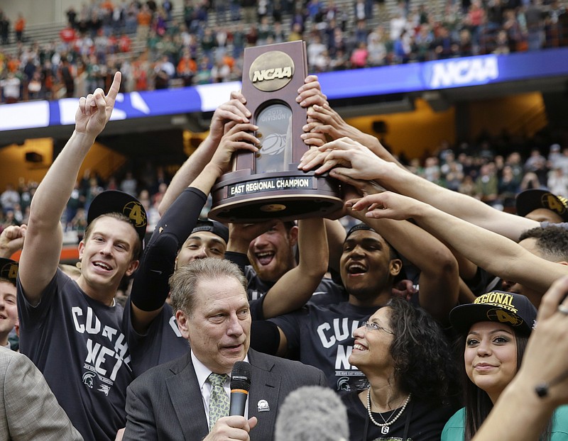 Michigan State players hold the East Regional championship trophy as coach Tom Izzo speaks after the regional final against Louisville in the NCAA men's college basketball tournament Sunday, March 29, 2015, in Syracuse, N.Y. Michigan State won 76-70.