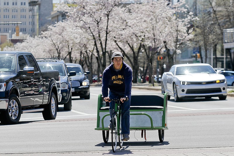 Chattanooga Bellhops mover and college student Nick Mattick pedals near the Tennessee Aquarium on Saturday looking for people to take on a cycle-rickshaw ride. Bellhops will offer free rides downtown on weekends through the summer as part of its internship program.