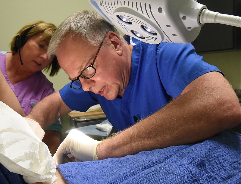 Assisted by LPN Grace Peters, who has worked with him for 14 years, Dr. David C. Redd removes a skin tag from patient Todd Shirley on Monday at QuikSurg on North Market Street.