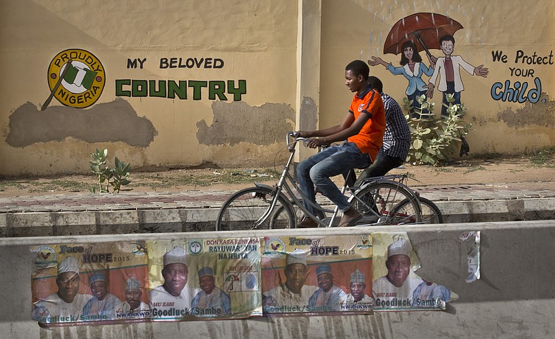 
              Two youths ride bicycles past a mural on a school wall and election posters supporting President Goodluck Jonathan, on a street in Kano, Nigeria Sunday, March 29, 2015. Voting in Nigeria's elections continued in certain areas on Sunday after technical problems prevented some people from casting their ballots on Saturday and despite extremist violence in the northeast and protests in the south. (AP Photo/Ben Curtis)
            