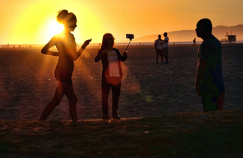 
              In this Friday, March 27, 2015 photo, a beachgoer using a cell phone on a stick snaps a selfie as the sun sets at Venice beach in Los Angeles. You can bring your beach towels and floral headbands, but forget that selfie stick if you’re going to the Coachella or Lollapalooza music festivals. The sticks are banned this year at the events in Indio, California, and Chicago. Coachella dismissed them as “narsisstics” on a list of prohibited items. (AP Photo/Richard Vogel)
            