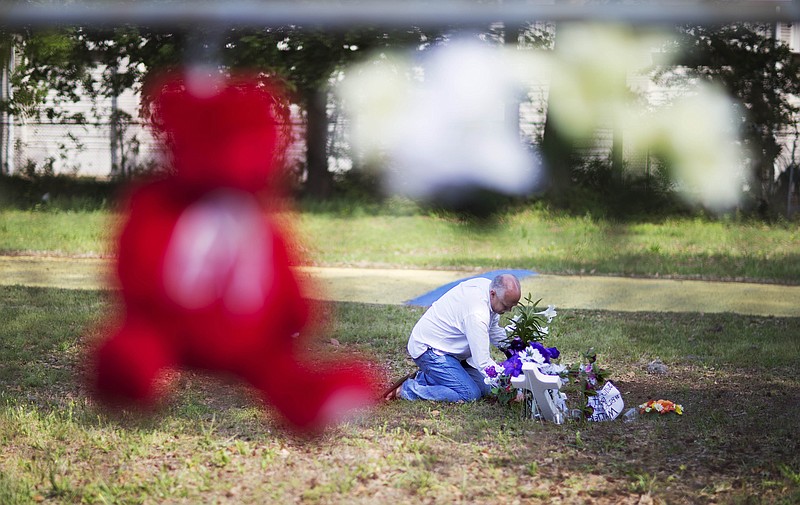 Jeffrey Spell, of Charleston, S.C., places flowers at the scene where Walter Scott was killed by a North Charleston police officer Saturday after a traffic stop as a teddy bear and flowers hang on the fence in North Charleston, S.C., on Thursday, April 9, 2015.