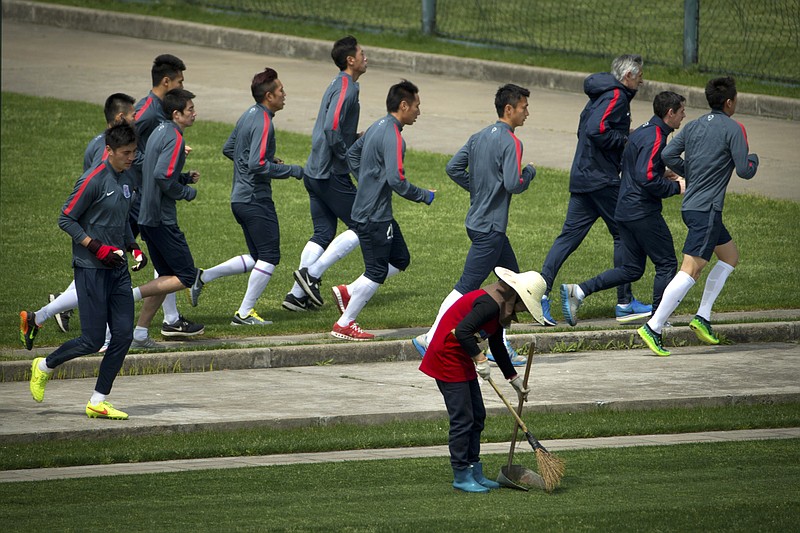 
              In this Thursday, April 9, 2015 photo, members of the Shanghai Shenhua soccer squad jog past a groundskeeper as they warm up during practice at the team's training facility in Shanghai. While a few years ago Chinese Super League (CSL) soccer was mired in corruption scandals and poor play, Shenhua is emblematic of the new and improved CSL - it’s increasingly globalized, brimming with newfound professionalism and flush with cash. (AP Photo/Mark Schiefelbein)
            