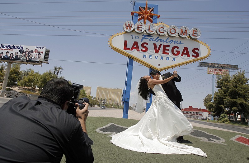 
              FILE - In this July 7, 2007, file photo, Wedding photographer Sergio Lopez, left, take pictures of newly-weds Joseph Buangan and his wife Joyce, both of Torrance, Calif., with the "Welcome to Fabulous Las Vegas" neon sign in the background in Las Vegas. Betty Willis, the woman who designed the iconic neon sign that has welcomed countless visitors to Las Vegas since 1959 has died. She was 91. (AP Photo/Jae C. Hong, File)
            