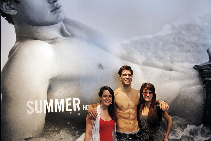In this May 25, 2011 file photo, an Abercrombie & Fitch employee, center, poses for photos with two customers at the entrance to the company's Fifth Avenue store, in New York. Abercrombie & Fitch Co. said Wednesday, Aug. 17, 2011, its second-quarter net income rose 64 percent, boosted by higher demand for its preppy fashions in the U.S. and Europe.(AP Photo/Mark Lennihan, File)