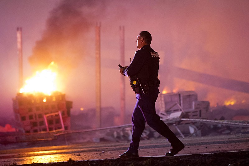 A police officer walks by a blaze Monday, April 27, 2015, after rioters plunged part of Baltimore into chaos, torching a pharmacy, setting police cars ablaze and throwing bricks at officers.