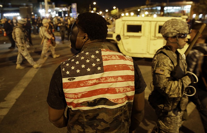 A protester watches soldiers pass as curfew approaches, Friday, May 1, 2015, in Baltimore. 
            