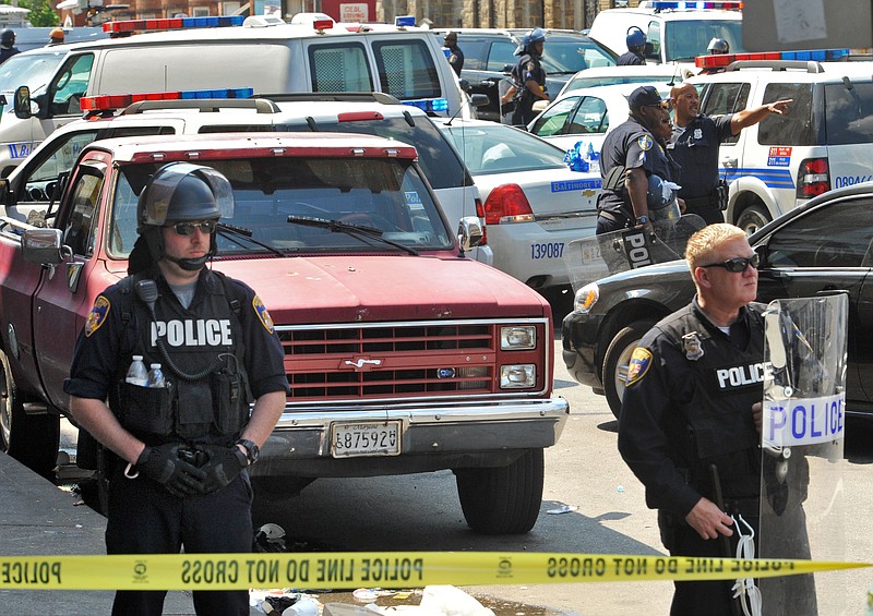 Police stand behind tape Monday, May 4, 2015, in Baltimore. Lt. Col. Melvin Russell said police pursued a man who was spotted on surveillance cameras and appeared to be armed with a handgun.