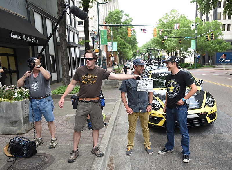 Six-time national cyclocross champion Tim Johnson, second from right, and Tanner Foust, right, professional racing driver, stunt driver and television host, stand in front of a Volkswagen GRC Beetle on Market Street on Monday while filming course previews that will air during the online broadcast of the USA Cycling National Championships, which take place in Chattanooga later this month. Jarrett Rawlings, second from left, and Brian Gilbert work on the Volkswagen America production.