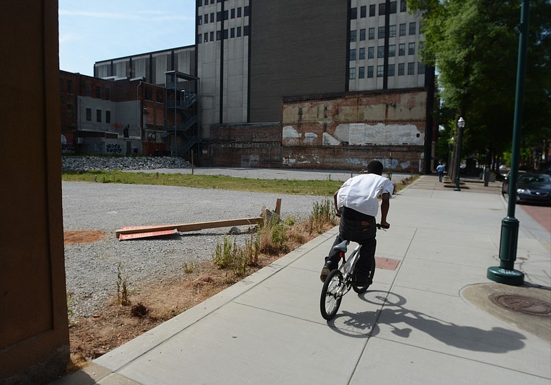 A man rides a bicycle on the sidewalk Thursday, May 14, 2015, in Chattanooga past a vacant lot in the 700 block of Market Street that was created when buildings were torn down 15 years ago for a project that did not materialize. 