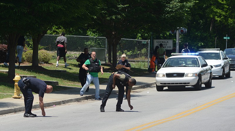 Chattanooga Police Officers Michael Holloway, left, and Robin Davenport place evidence markers at the scene of a midday shooting on E 38th Street that left one person with non life-threatening injuries on Wednesday, May 20, 2015, in Chattanooga, Tenn.