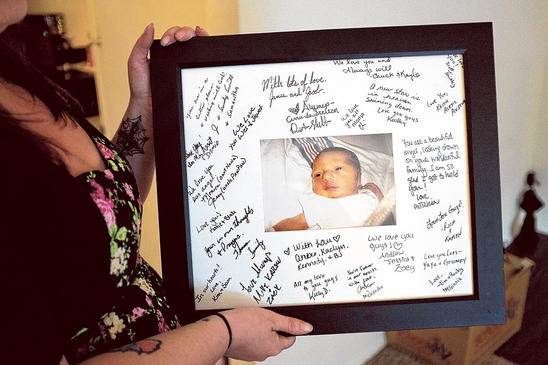 Emily Mitchell holds a photo of her deceased son, Lucian, signed by visitors to his memorial service.