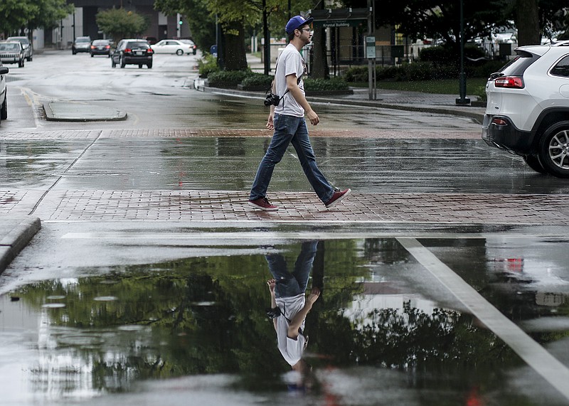 A pedestrian is reflected in a puddle as he crosses Broad Street at Martin Luther King Jr. Boulevard during afternoon rain showers Tuesday, May 26, 2015, in Chattanooga.