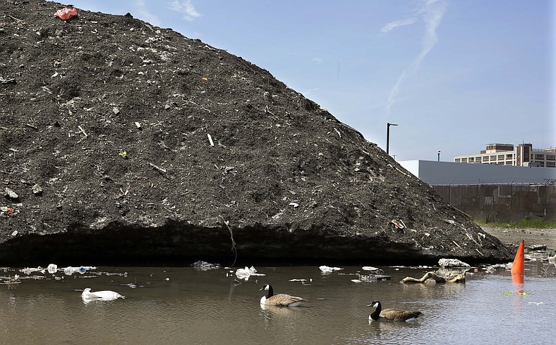 
              Canada geese swim beneath a debris-covered snow pile, lingering after the record-setting winter, Thursday, May 28, 2015, the Seaport District in Boston. A 75-foot-high snow mound in the Seaport District has been reduced to a three-story pile of dirt and trash, including bicycles, traffic cones and even half a $5 bill, that remains encrusted in solid ice. Crews have been working for six weeks to clean away the trash as it breaks free from the mound. So far, they have pulled 85 tons of debris from the pile. (AP Photo/Elise Amendola)
            