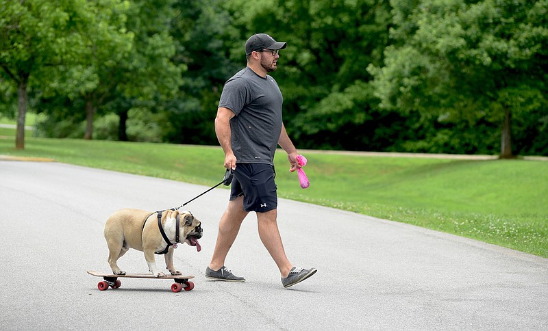 Dr. Corey Idrogo walks at Greenway Farm on Monday in Chattanooga with his dog, Nucky, who uses a skateboard. Idrogo says his dog not only likes to ride on the skateboard, he likes to chew on it, too.