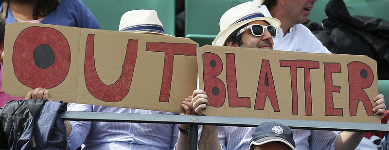 Two spectators hold signs reading "Out Blatter", referring to newly re-elected FIFA president Sepp Blatter during the French Open tennis tournament between Spain's Garbine Muguruza and Lucie Safarova of the Czech Republic at the Roland Garros stadium, in Paris on June 2, 2015. 