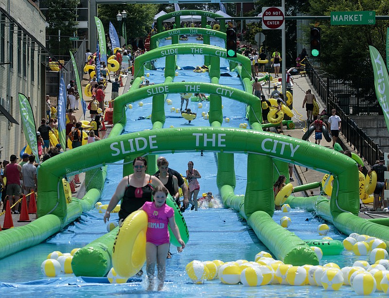 Sliders reach the bottom of the 5th street hill during the Slide the City water slide event Saturday, June 20, 2015, in Chattanooga, Tenn. A 1,000 foot water slide was set up on 5th street downtown for the event.