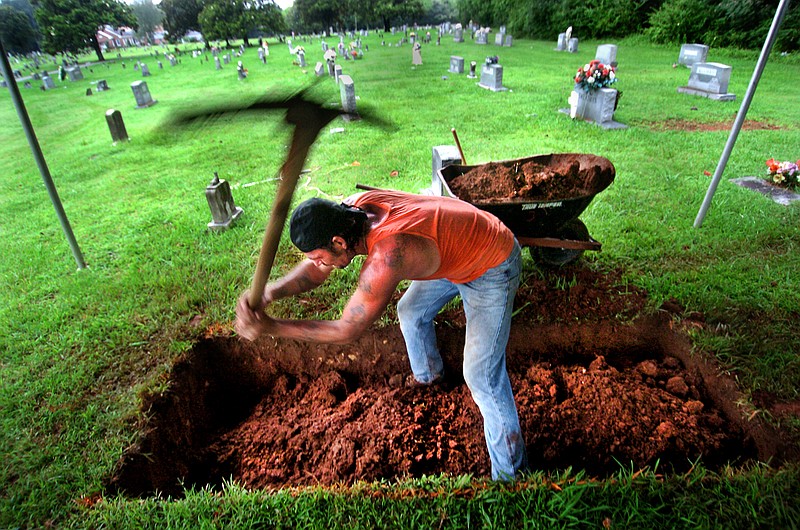 In this 2005 photo, Johnny "Digger" Tucker uses a pick ax to break up the soil and rock while digging a grave at the Old Trion Cemetery in Trion, Ga. Grave digging is a family business for the Tucker family.