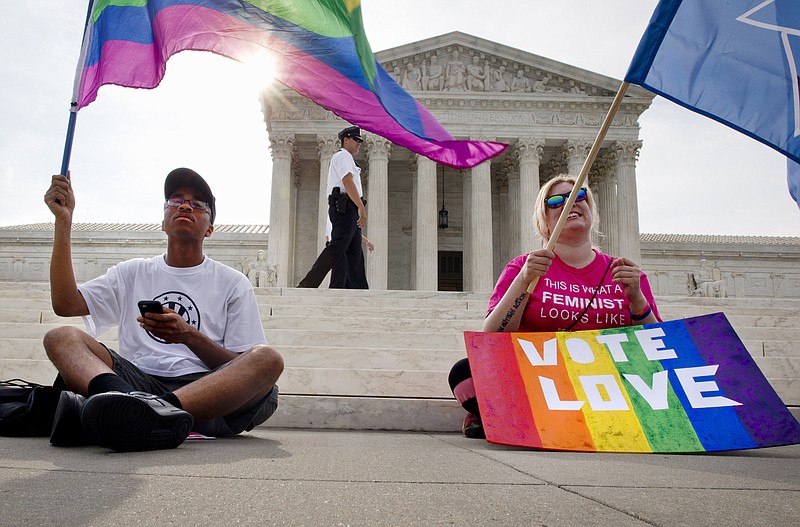 Carlos McKnight, 17, of Washington, left, and Katherine Nicole Struck, 25, of Frederick, Md., hold flags in support of gay marriage as security walks behind outside of the Supreme Court in Washington, Friday June 26, 2015. 