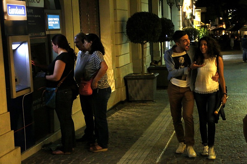 A couple passes by the ATM machines used by people in Monastiraki in Athens, early Monday, June 29, 2015. 