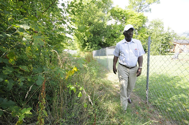 Staff photo by Tim Barber
Alton Park resident Milton Jackson, 79, walks behind homes in his neighborhood where he says overgrown alleyways help conceal areas for crime.