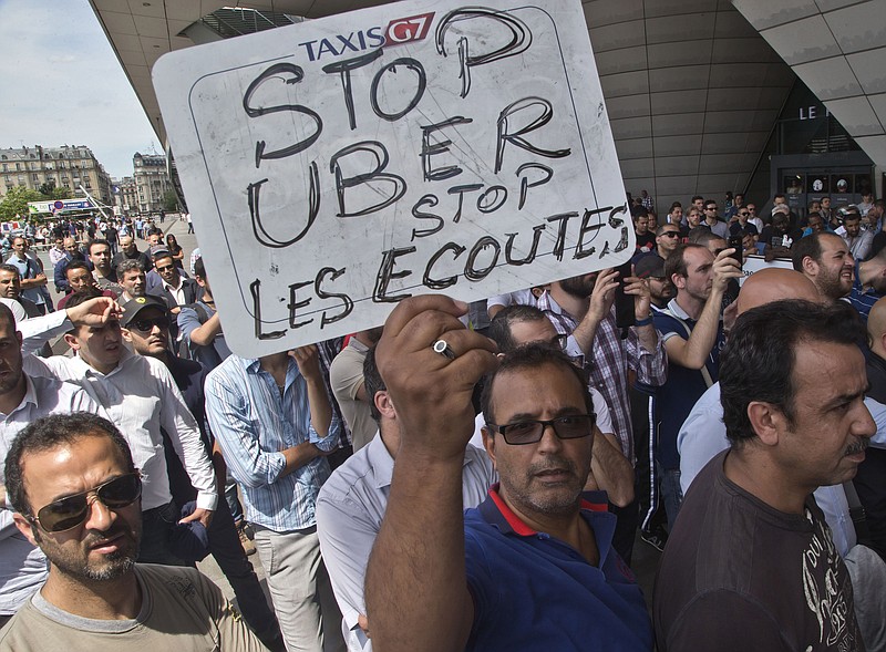 
              FILE - This Thursday, June 25, 2015 file photo shows a striking taxi driver holding a placard which read, "Stop Uber, Stop listening," referring to the new US spying report in France, during a taxi drivers demonstration in Paris, France. French authorities took two Uber managers into custody for questioning on Monday over "illicit activity" involving its low-cost service. The detentions came amid rising tensions between the government and the ride-hailing company, which culminated last week in a violence-marred taxi strike that blocked roads around the country. (AP Photo/Michel Euler, File)
            