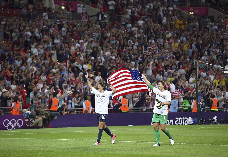 Carli Lloyd, left, and Hope Solo, of the U.S. women's soccer team, with the American flag after their team won the gold medal match against Japan at the 2012 Summer Olympic Games, in London, Aug. 9, 2012. (Doug Mills/The New York Times)
