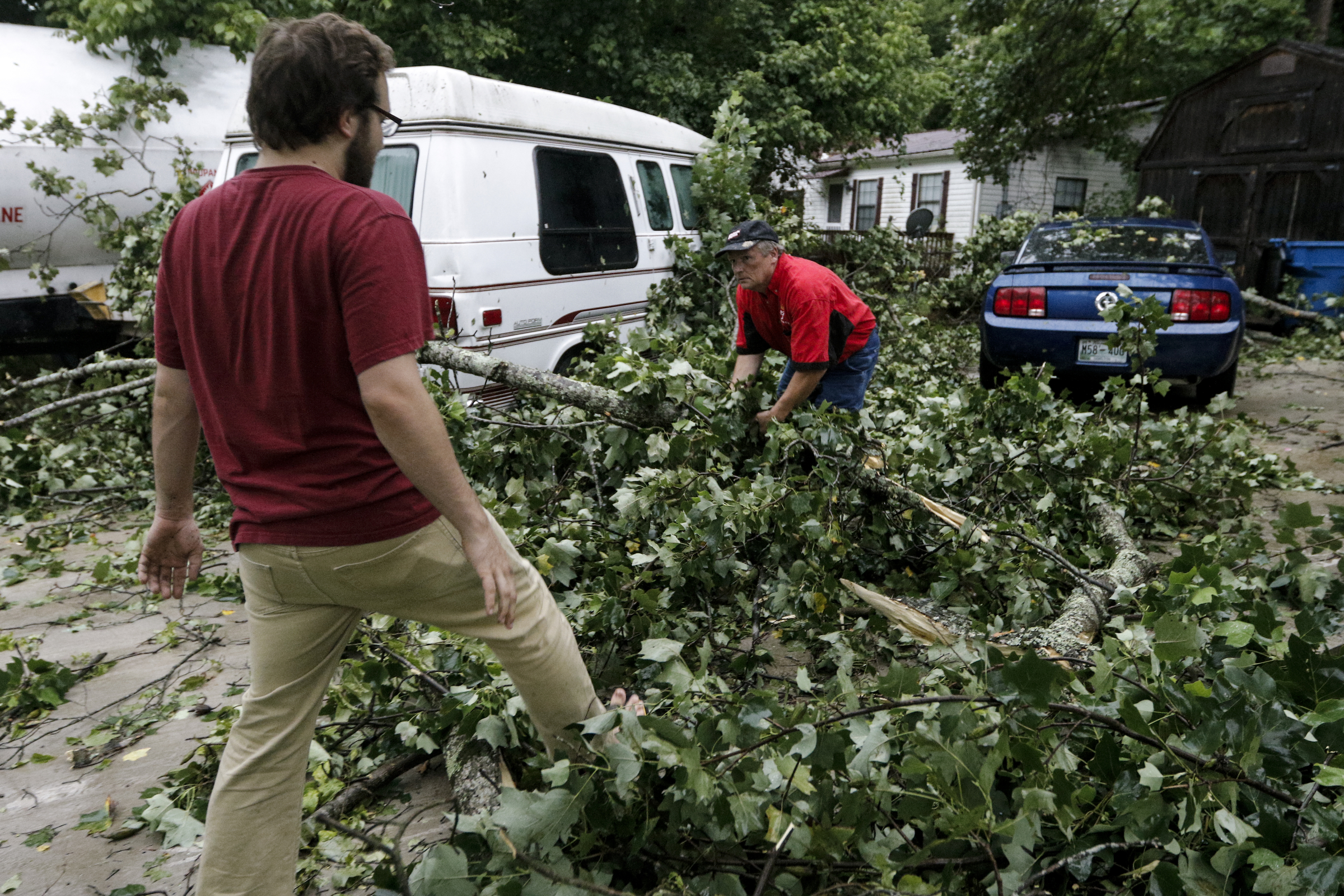 Chris Ridge, left, and his father Mike clear a downed tree that fell on their Mustang in the driveway of their home on Lullwater Road after heavy thunderstorms swept through the region Tuesday, July 14, 2015, in Red Bank, Tenn.