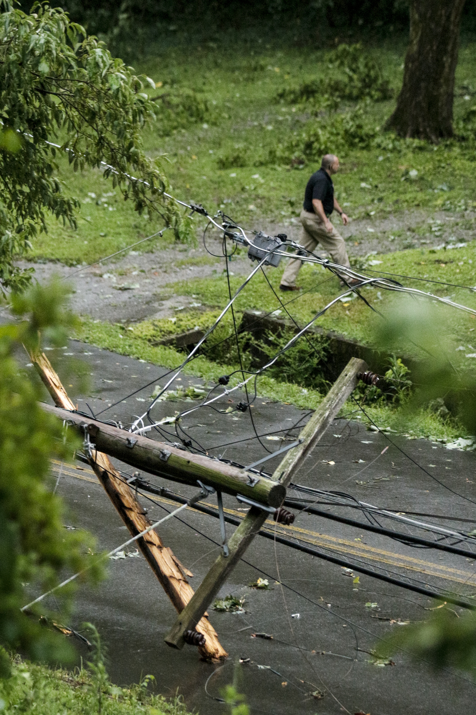 An emergency responder walks near a snapped utility pole brought down by a tree after heavy thunderstorms swept through the region Tuesday, July 14, 2015, in Red Bank, Tenn.