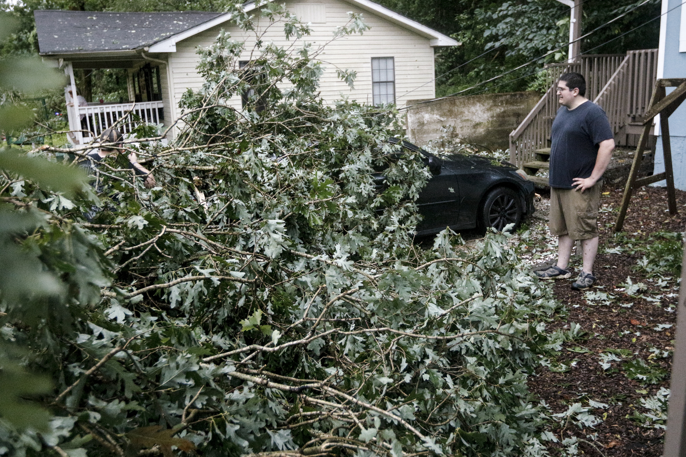 Nathan Chubbuck looks at a downed tree on top of a car next to a home on Hedgewood Drive after heavy thunderstorms swept through the region Tuesday, July 14, 2015, in Red Bank, Tenn.