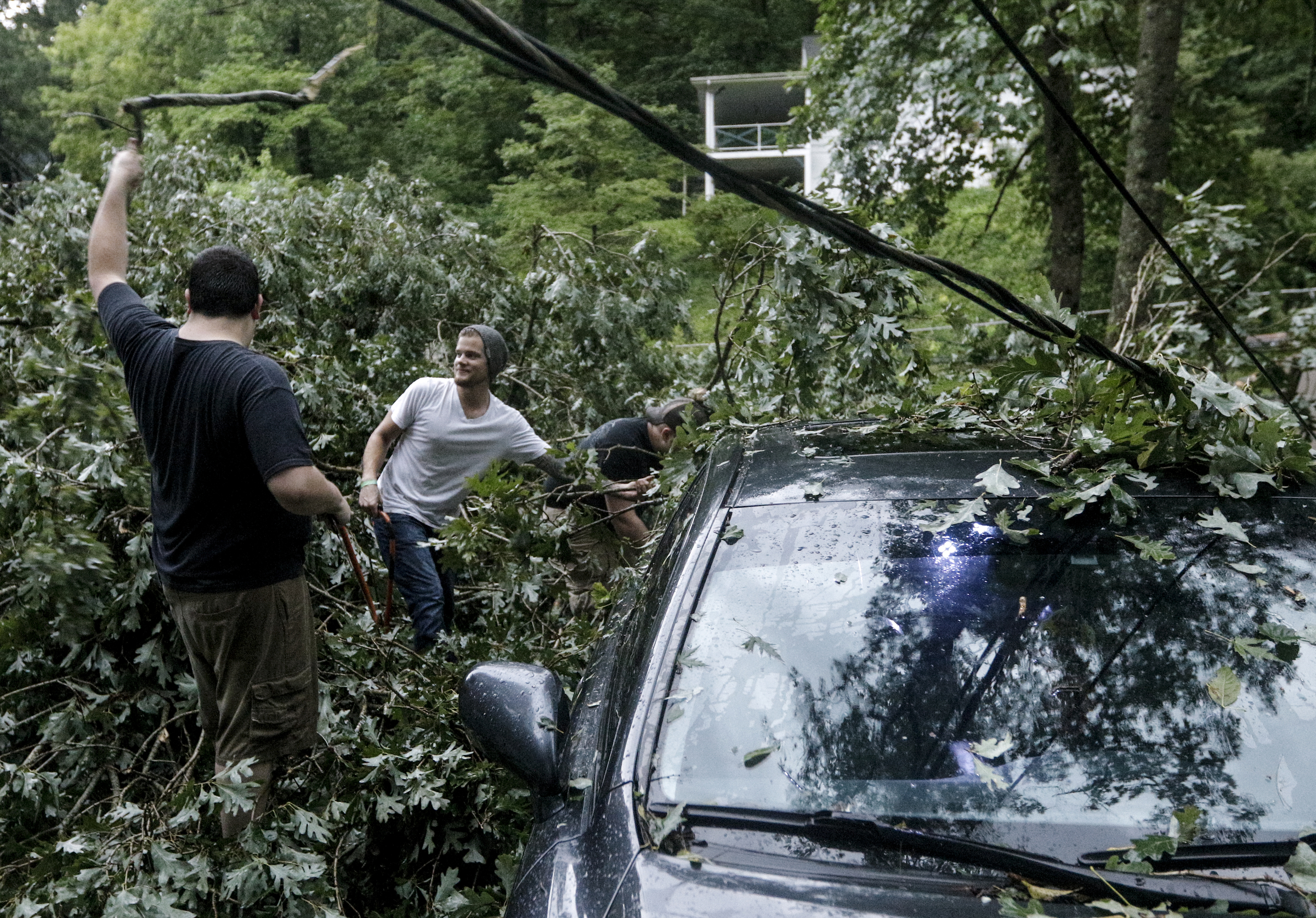 Nathan Chubbuck, Gage Hahn, and David Slaney, from left, clear a downed tree from a car in the yard of a home on Hedgewood Drive after heavy thunderstorms swept through the region Tuesday, July 14, 2015, in Red Bank, Tenn.