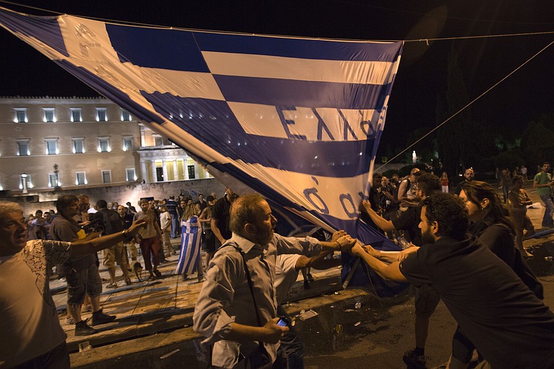 Protesters scuffle with each other to tear down a Greek flag with a writing reading ''Greece we love you'' during a rally outside the Greek Parliament in Athens on Wednesday, July 15, 2015. 