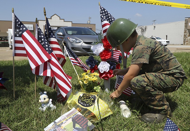 Staff Photo by Dan Henry / Five-year-old Eli Arnold places a small flag at a makeshift memorial in front of the Armed Forces Career Center off of Lee Highway where a shooting spree began leading to the death of four Marines.