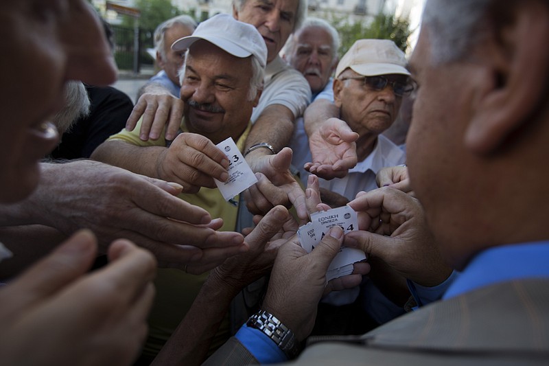 A bank employee distributes tags with queue positions to pensioners as they wait outside the main gate of the national bank of Greece in central Athens last week to withdraw a maximum of 120 euros ($134).