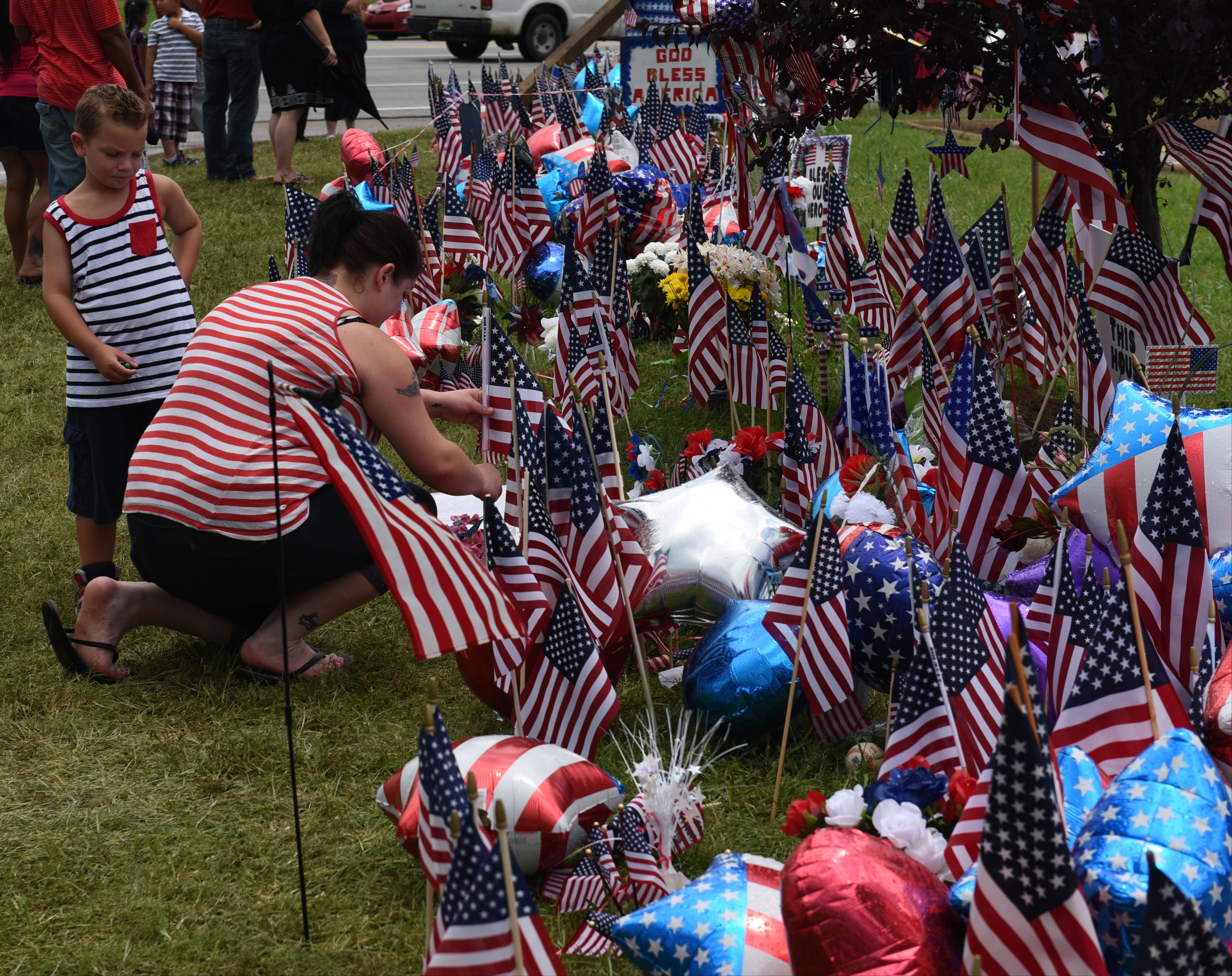 Isaac Pierce watches his mother, Stefanie Pierce, as she straightens a flag at a makeshift memorial in front of the Armed Forces Career Center on Lee Highway on Sunday, July 19, 2015, in Chattanooga, Tenn. The memorial began in the aftermath of a Thursday terrorist attack that killed four Marines and one member of the U.S. Navy.