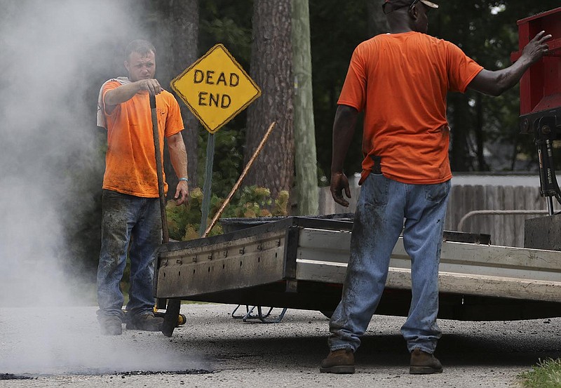 Workers with Jarrett Builders Gary Shoot and Charles McDaniel, from left, wait for the roadbed to heat up while repairing the asphalt off of West 42nd Street in St. Elmo on Tuesday.