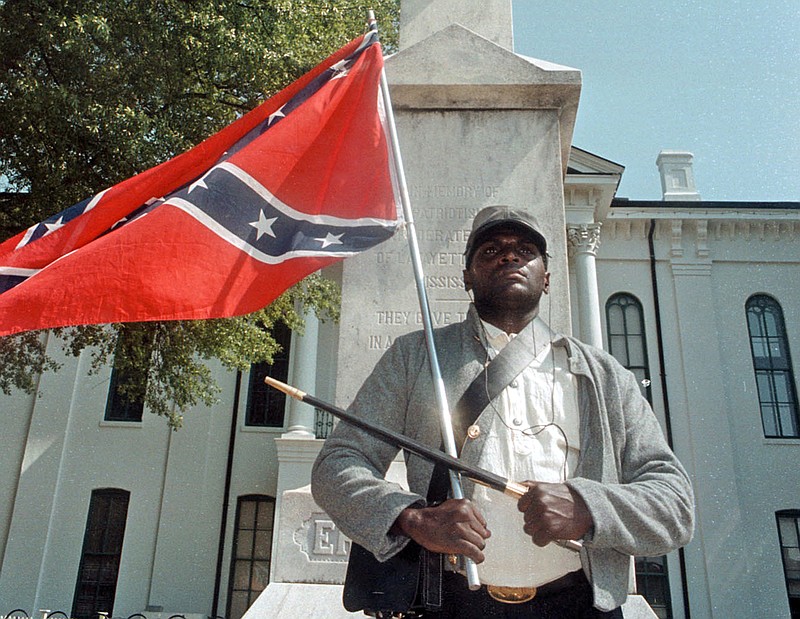 
              FILE - In this May 8, 2000, file photograph, Anthony Hervey holds a Confederate flag while standing underneath the Confederate monument in Oxford, Miss. The Highway Patrol says 49-year-old Hervey was killed Sunday, July 19, 2015, when his 2005 Ford Explorer left the roadway and overturned on Mississippi Highway 6 in Lafayette County. Hervey, of Oxford, has drawn attention over the years for opposing efforts to change the flag. He said he dressed in Rebel soldier garb to honor blacks who served with the Confederacy during the Civil War. (Bruce Newman/The Oxford Eagle via AP, File)
            