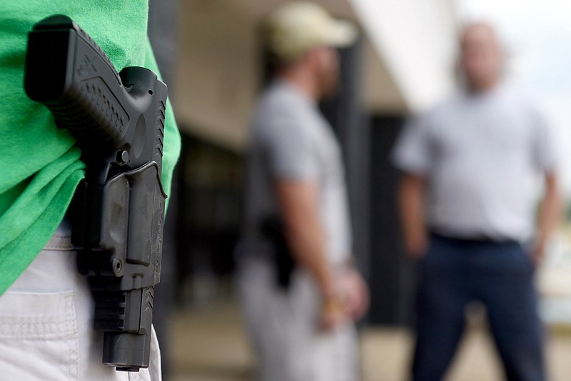 In this photo taken Monday, July 20, 2015, a man who would only give his name as J.R., from Norfolk, Va., stands with his sidearm as dozens of people, some armed with weapons and some carrying water, to the front door of the Armed Forces Career Center in Huntsville, Ala. Armed civilians patrolled the sidewalk and parking lot in front of the storefront recruiting center after five service members were killed by a lone assailant in Chattanooga, Tenn. (Eric Schultz/AL.com via AP) 
