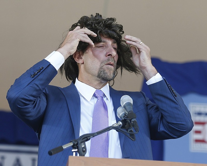 Former Atlanta Braves pitching great John Smoltz puts on a wig as he speaks during his induction to the Baseball Hall of Fame on Sunday in Cooperstown, N.Y.