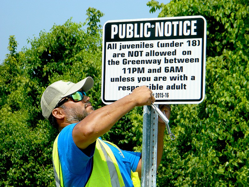 Please Haruo, a signs and markings technician with Cleveland's Public Works Department, posts a new ordinance that prohibits juveniles under the age of 18 years of age to be on the city's greenway between 11 p.m. and 6 a.m. unless they are accompanied by a responsible adult.
