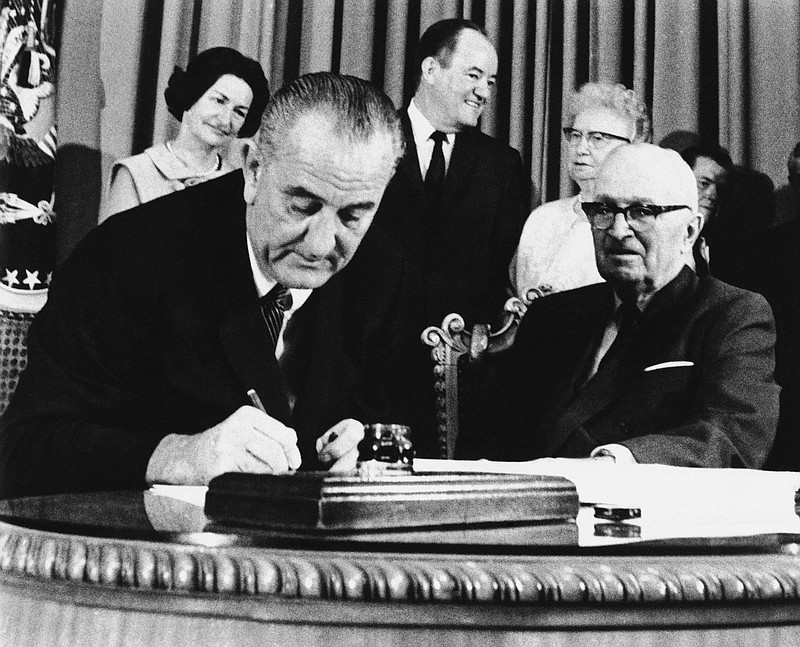 In this July 30, 1965, file photo, President Lyndon Johnson signs the Medicare Bill into law while former President Harry S. Truman, right, observes during a ceremony at the Truman Library in Independence, Mo. At rear are Lady Bird Johnson, Vice President Hubert Humphrey, and former first lady Bess Truman. When Johnson signed Medicare and Medicaid into law Americans 65 and older were the age group least likely to have health insurance.