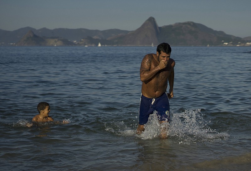 In this July 12, 2015, photo, a man wipes his face as he wades through the waters of the Marina da Gloria in Rio de Janeiro, Brazil.