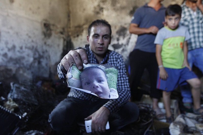 A relative holds up a photo of a one-and-a-half year old boy, Ali Dawabsheh, in a house that had been torched in a suspected attack by Jewish settlers in Duma village near the West Bank city of Nablus on Friday, July 31, 2015.