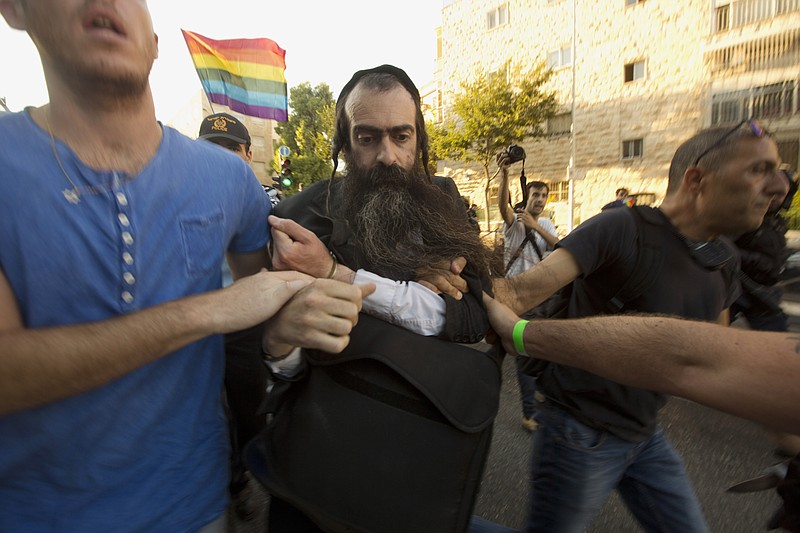 
              FILE - In this Thursday, July 30, 2015 file photo, ultra-Orthodox Jew Yishai Schlissel is detained by plain-clothes police officers after he stabbed people during a gay pride parade in Jerusalem. An Israeli hospital spokeswoman said Sunday, Aug. 2, that a teenage girl stabbed by Schlissel, an anti-gay extremist, in Thursday's attack during the parade has died. (AP Photo/Sebastian Scheiner, File)
            