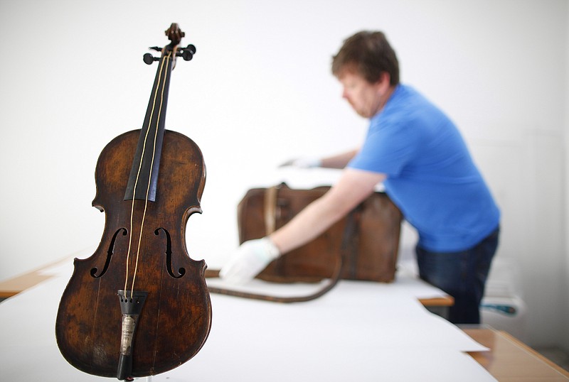 
              FILE - In this Sept. 16, 2013 file photo, Sean Madden, of Fine Art Conservation, works to show the violin played by bandmaster Wallace Hartley during Titanic's tragic maiden voyage, during a photocall to the media in Lurgan, Northern Ireland. The sea-corroded violin believed to have been played by the bandmaster of the Titanic as the ocean liner sank will be displayed next year at a pair of U.S. museums; from March 7 to May 29 in Branson, Missouri, and from June 5 to Aug. 14 in Pigeon Forge, Tennessee.  (AP Photo/Peter Morrison, File)
            