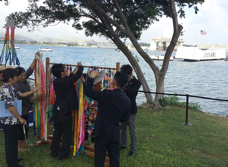 
              People hang paper cranes folded for peace near a memorial to the sunken battleship USS Arizona before a ceremony marking the 70th anniversary of the end of World War II, Friday, Aug. 14, 2015, in Pearl Harbor, Hawaii. Mayors and city council members from Honolulu and Nagaoka, Japan, joined the U.S. Pacific Fleet commander to lay wreaths and unveil a new plaque. (AP Photo/Audrey McAvoy)
            